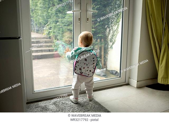 Baby girl with schoolbag looking through door