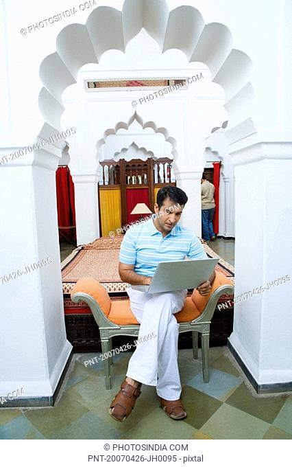 Mid adult man sitting on a couch and using a laptop