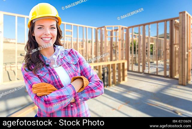 Young attractive female construction worker wearing gloves, hard hat and protective goggles at construction site