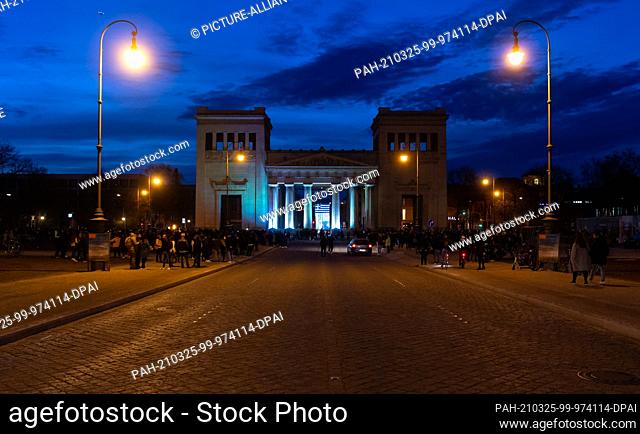 25 March 2021, Bavaria, Munich: A light installation illuminates the Propylaea on Königsplatz in the colours white and blue