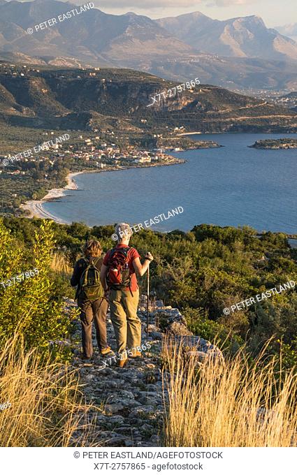 Walkers on a Kalderimi, stone path, above the Outer Mani coast looking down on Kardamyli (centre) with theTaygetos mountains in the background, , Messinia