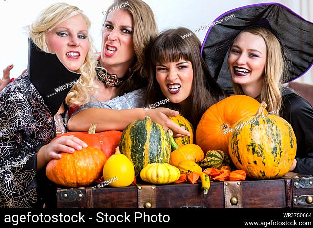 Four cheerful beautiful women toasting while celebrating Halloween together during costume party indoors in a decorated room