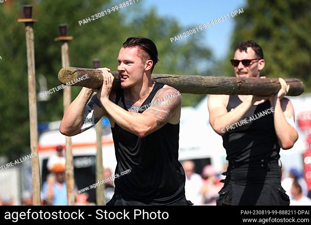 19 August 2023, Baden-Württemberg, Horgenzell: Participants of the 11th Upper Swabian Highland Games run in a slalom with a wooden pole in the discipline...
