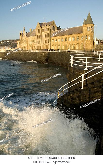 wave crashing on sea wall by the old college building, aberystwyth university, wales UK
