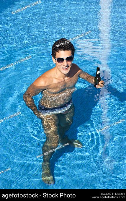 Hispanic man drinking beer in swimming pool