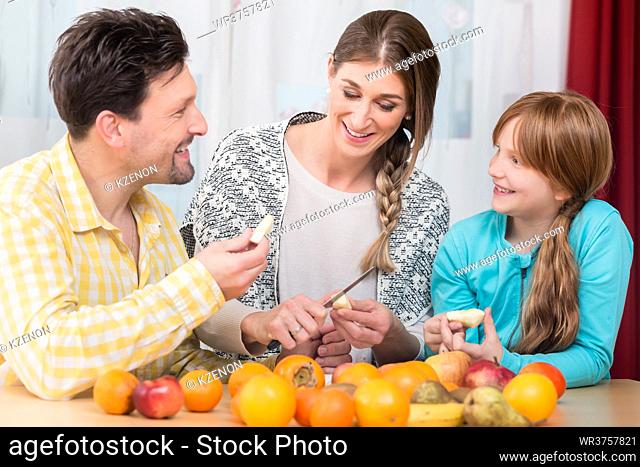 Portrait of smiling woman cutting healthy fruits with knife for her husband and daughter