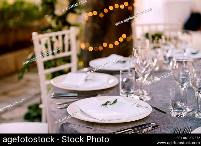 White round plates on a round table with gray tablecloth, white Chiavari chairs with white pillows. A floral arrangement in the center of the table