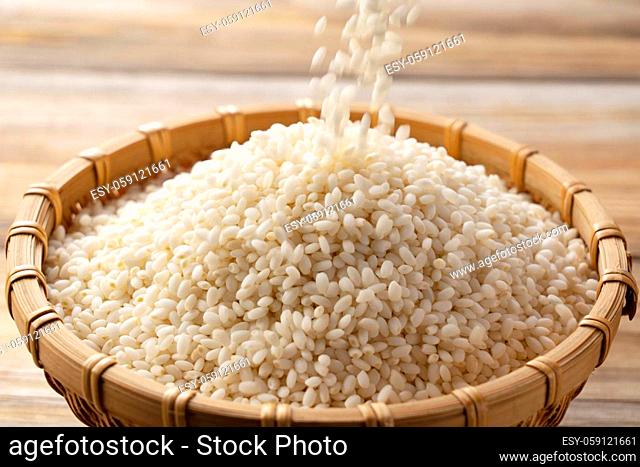 Close-up of the moment glutinous rice is poured into a bamboo colander set against a wooden background