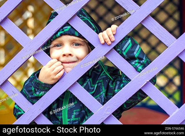 Cute little baby boy looking through blue fence