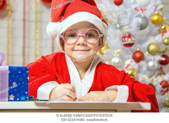 Four-year girl dressed in a red suit Santa Claus draws pencils are in a festive Christmas interior