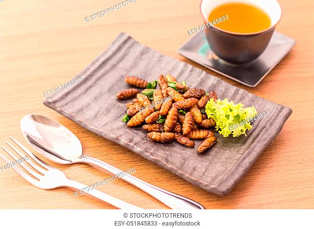 Fried insects - Wood worm insect crispy with pandan after fried and add a light coating of sauce and garnish Thai pepper powder with fork and spoon, tea