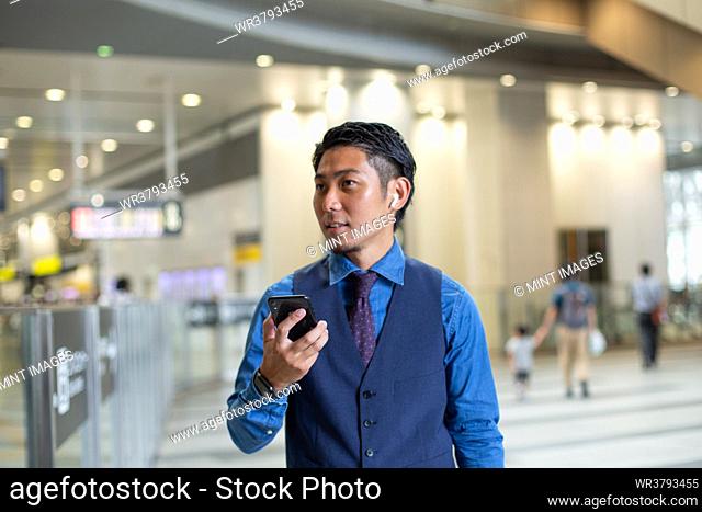 A young businessman in the city, on the move, at a transport hub, holding his phone and looking around