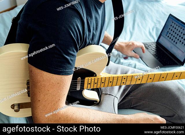 Man learning to play electric guitar online using laptop