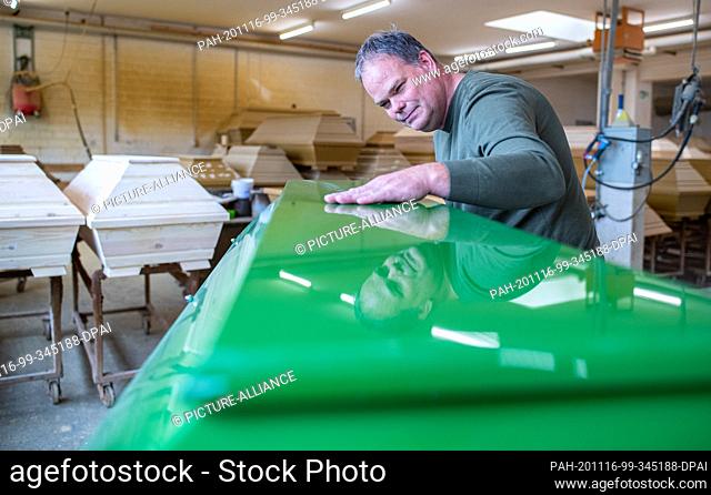 12 November 2020, Lower Saxony, Glandorf: Udo Mentrup, Managing Director of the coffin manufacturer Schmidt-Hendker, stands at a coffin and is reflected in the...