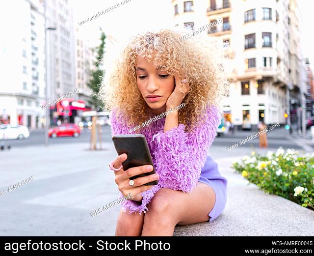 Young woman with afro hairstyle using smart phone in city