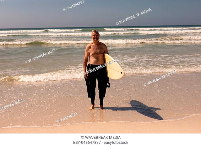Front view of senior male surfer standing with surfboard on the beach