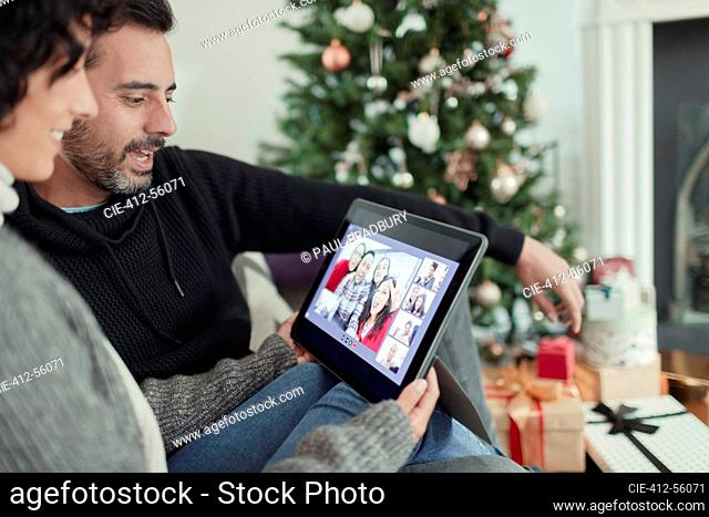 Happy couple video chatting with family on digital tablet at Christmas