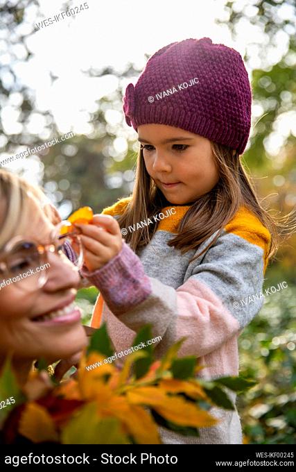 Girl putting leaf in smiling woman's hair