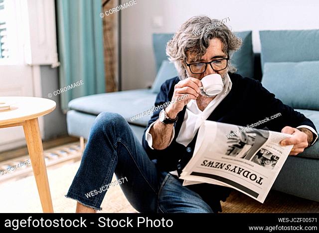 Senior man having coffee reading newspaper while sitting at home