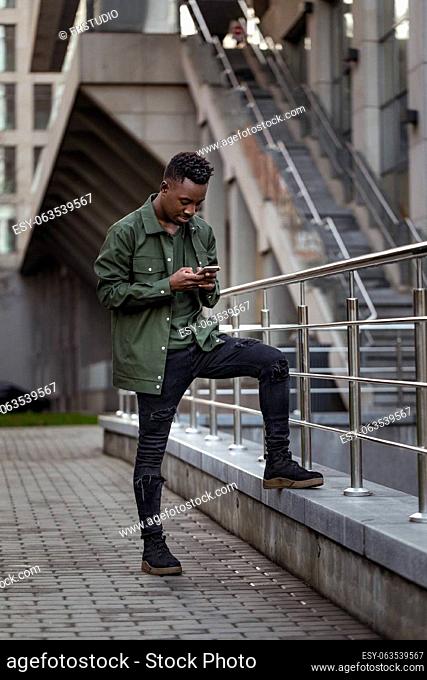 young african american man in jacket messaging online, checking social networks outdoor