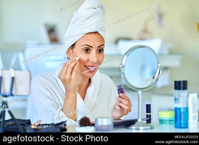 Female influencer applying serum while vlogging through smart phone at home