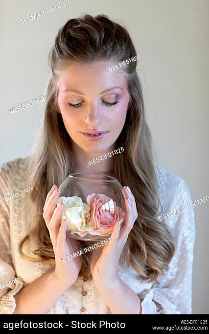 Young woman smelling scented roses in bowl at studio