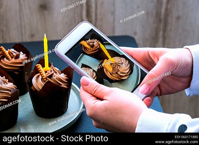 Female hands taking photo of Delicious chocolate cupcakes with cream on dark background. Influencer Three chocolate muffin