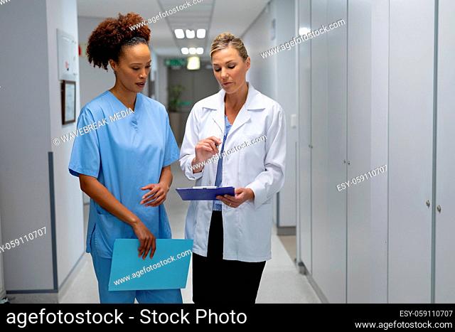 Two diverse female doctors standing in hospital corridor looking at medical chart document