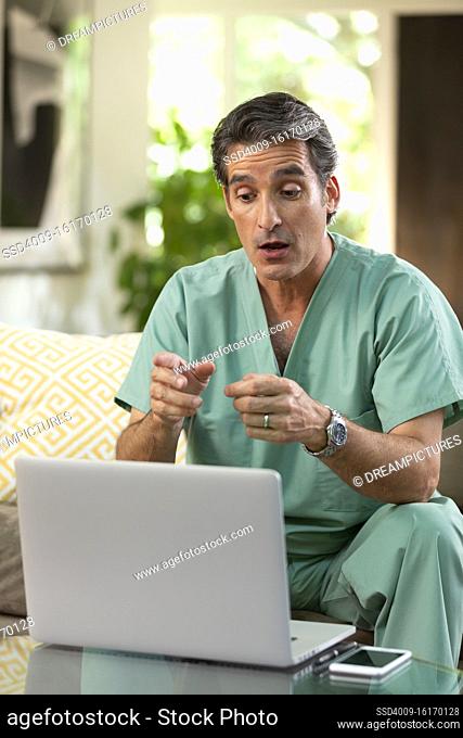 Hispanic Male doctor practicing tele-medicine from his home using laptop computer to consult patient on video call