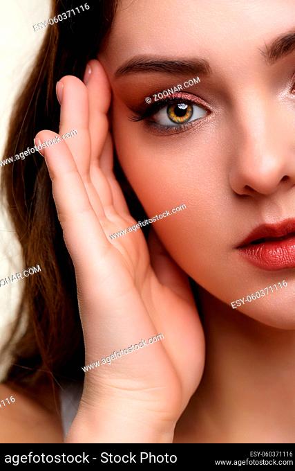 Beauty portrait of young woman with hand near face. Brunette girl with evening female makeup touches face