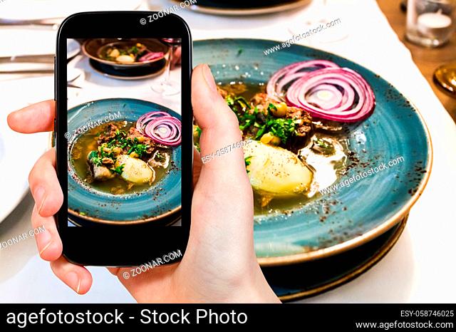 travel concept - visitor photographs of traditional caucasian soup Putuk (Piti) from mutton brisket, chick peas, potatoes in plate on smartphone