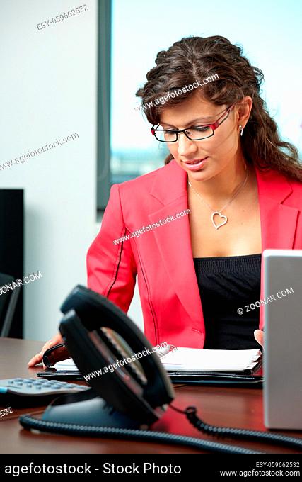 Young businesswoman sitting at desk in office, looking at personal organizer