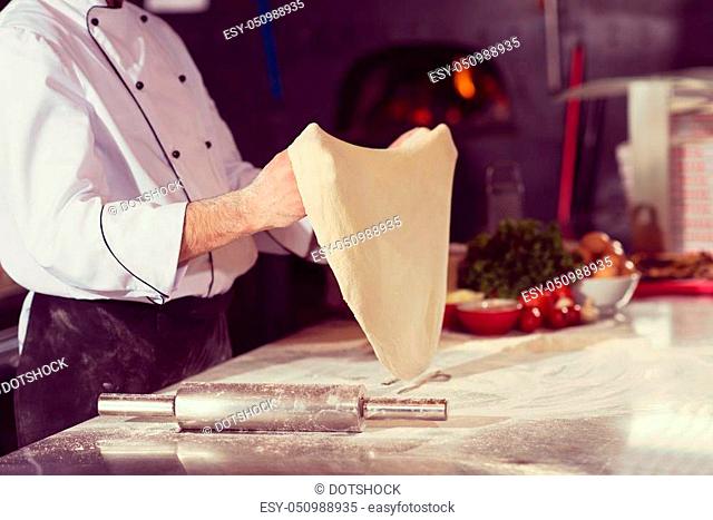 Skilled chef preparing dough for pizza rolling with hands and throwing up