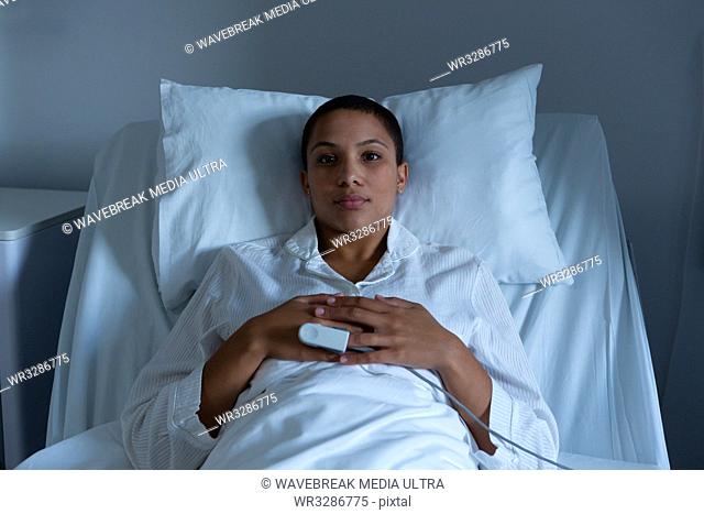 Portrait of beautiful young mixed race female patient lying on bed with hands on stomach in the ward in hospital. Pulse oximetry is measuring the oxygen level...