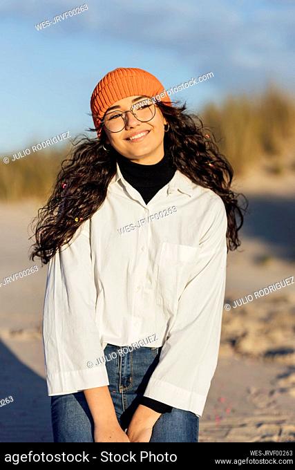 Smiling woman in eyeglasses against sky looking away at beach