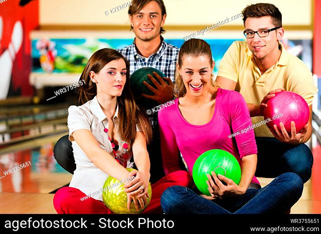Group of four friends in a bowling alley having fun, holding their bowling balls