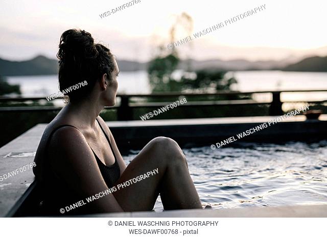 Philippines, Palawan, Coron, woman sitting in swimming pool in the evening
