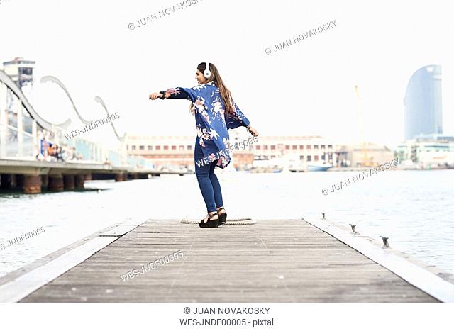 Spain, Barcelona, happy young woman with headphones dancing on jetty
