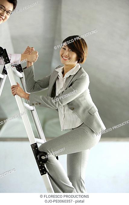 Businessman helping businesswoman up ladder in structure