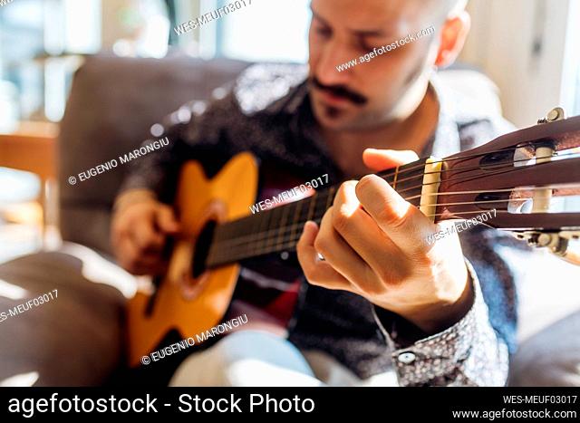 Young male guitarist playing guitar at home