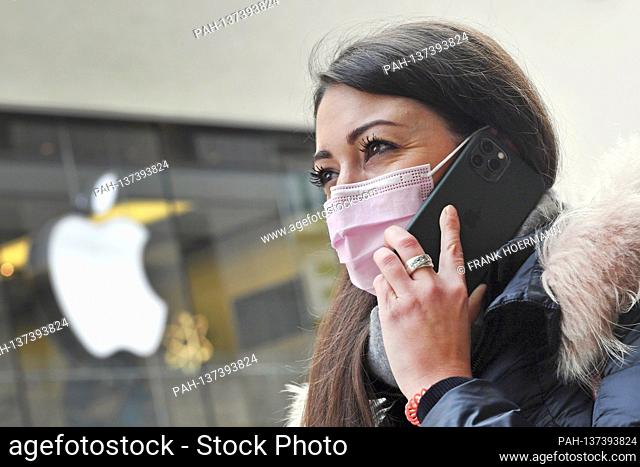 Mask compulsory in the pedestrian zones and public places in Munich on November 16, 2020. Young woman with an everyday mask is on the phone with her Apple...