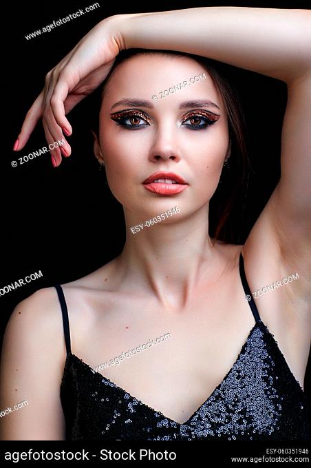 Beautiful young woman portrait with vogue shining face makeup and eye shadows with golden sparcles. Female dressed in black dress with straps and sequins