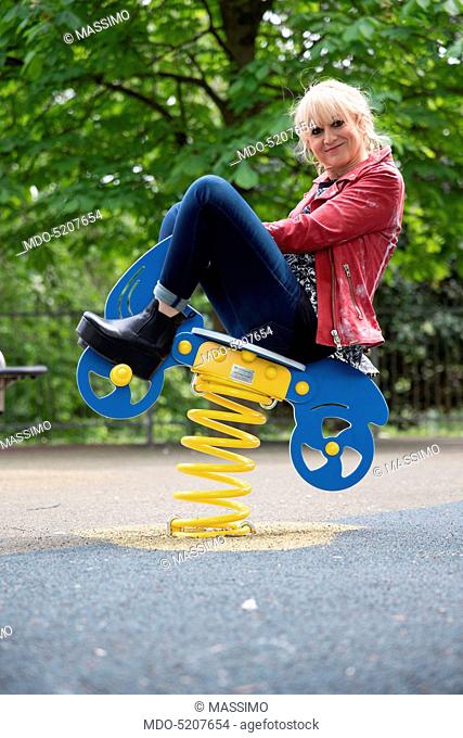 Actress and comedian Luciana Littizzetto sitting on a spring toy horse in a playground inside the public park Parco del Valentino. Turin, Italy