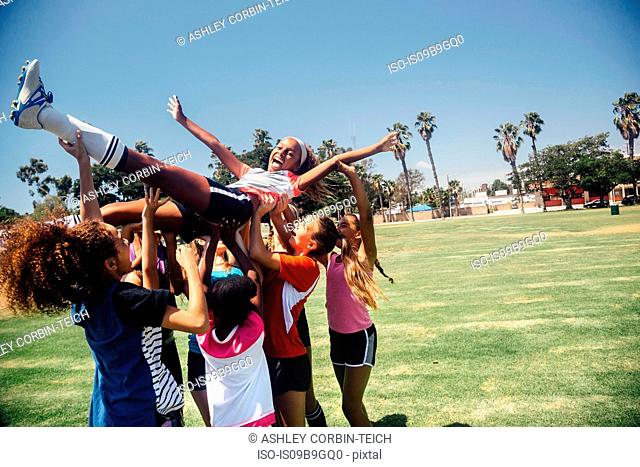 Schoolgirl soccer team carrying player above their heads on school sports field