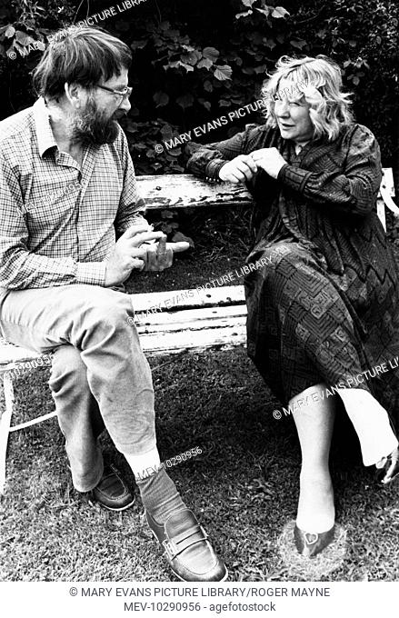 Fay Weldon, author, essayist and playwright, in conversation with the novelist John Fowles (1926-2005) in 1983. They are sitting on a bench in a garden