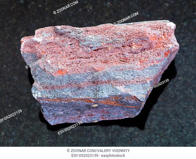 macro shooting of natural mineral rock specimen - raw jaspilite (ferruginous quartzite) stone on dark granite background