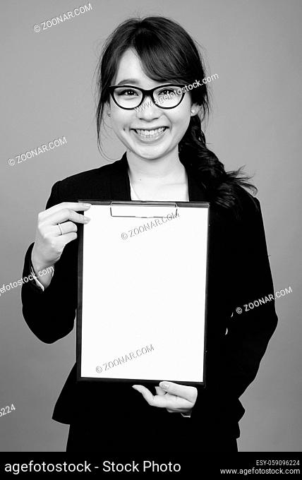 Studio shot of young beautiful Asian businesswoman wearing eyeglasses against gray background in black and white