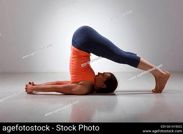 Beautiful sporty fit yogini woman practices yoga asana Halasana - plow pose