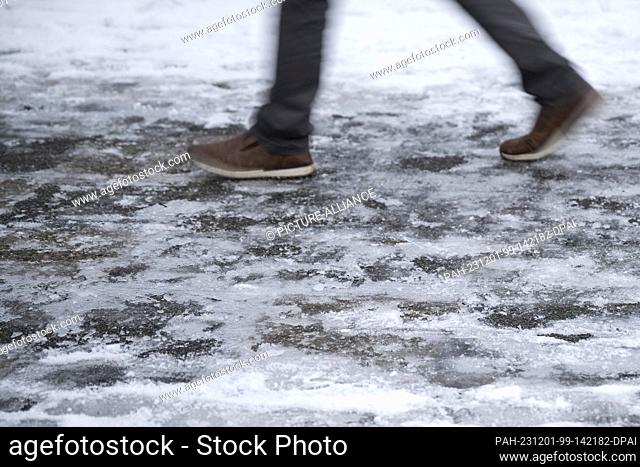 PRODUCTION - 30 November 2023, Berlin: A person walks on an icy sidewalk. The consequences of the winter weather in Berlin are slippery roads and sidewalks