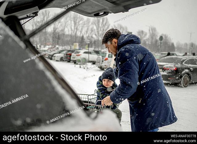 Father with son sitting in shopping cart at snowy parking lot